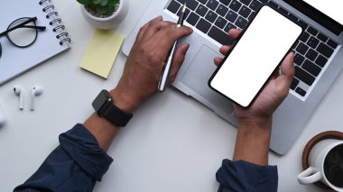 İş adamı akıllı telefon tutuyor ve iş yerinde dizüstü bilgisayar kullanıyor..