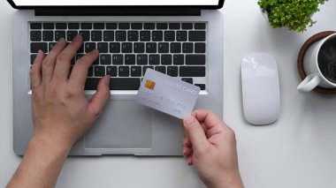 Kredi kartı tutan ve online ödeme yapmak için dizüstü bilgisayar kullanan bir adam..