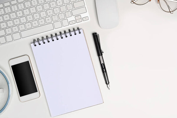 Above view white office desk with empty notebook, smart phone, glasses and pen.