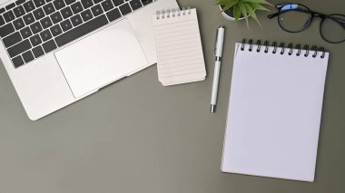 Yeşil arka planda dizüstü bilgisayar, defter ve ev bitkisi.