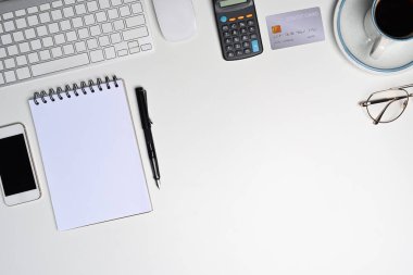 Not defteri, hesap makinesi, cep telefonu ve gözlüklü üst görünüm beyaz ofis masası.
