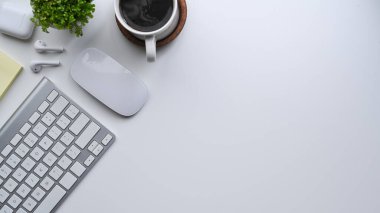 Kablosuz klavyesi, kahve fincanı ve saksısı olan beyaz ofis masası..