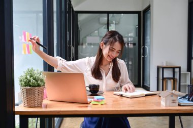 Dizüstü bilgisayarla çalışan gülümseyen kadın çalışanlar ve ofisteki cam duvardaki yapışkan notları not edenler..