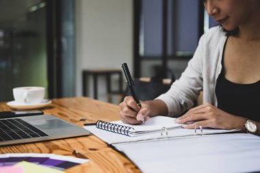 Genç bir bayan ofis masasında otururken not alıyor..