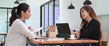 İki bayan meslektaşım ofiste yeni proje başlatma fikirleri hakkında konuşuyor..