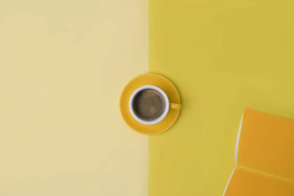 Above view a cup of coffee and notebook on yellow background.