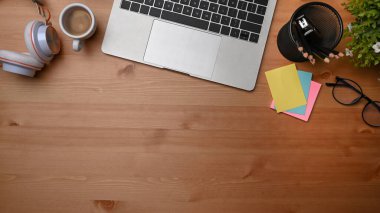 Dizüstü bilgisayar, yapışkan not, kulaklık ve kahve fincanı ahşap masada..