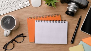 Boş defter, kahve fincanı, bardaklar, kamera ve cep telefonu ahşap masada..