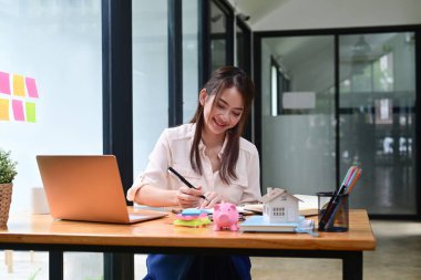 Ofis masasında oturup dizüstü bilgisayarla çalışan mutlu kadın ofis çalışanı..