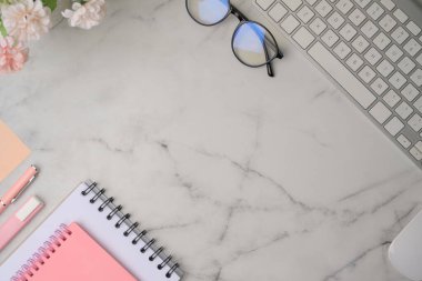 Mermer zemin üzerinde gözlük, defter ve çiçeklerle üst görünüm kadın çalışma alanı.
