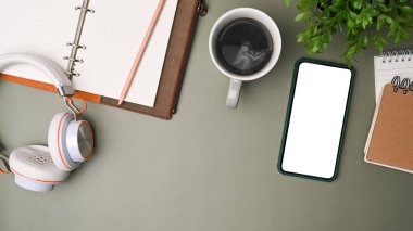 Üst görünüm cep telefonu, kulaklık, kahve fincanı ve gri arka plandaki defter gibi..