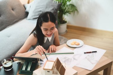 Gülümseyen kadın mimar planlar üzerinde çalışıyor ve evde bilgisayar tableti kullanıyor..
