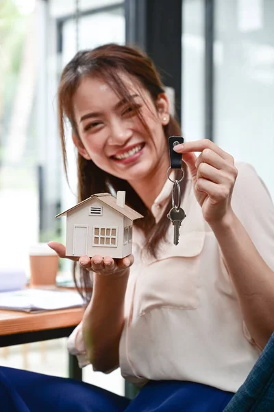 Real estate agent woman holding white house model and house key in hand.