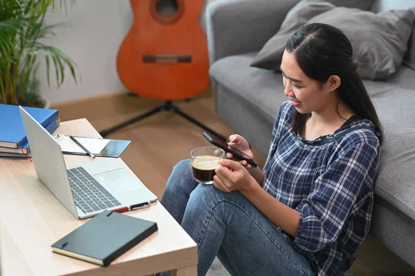 Ung Hona Som Håller Kaffekopp Och Använder Mart Telefon Vardagsrummet — Stockfoto