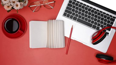 Kırmızı arkaplanda dizüstü bilgisayar, defter ve kahve fincanı var..