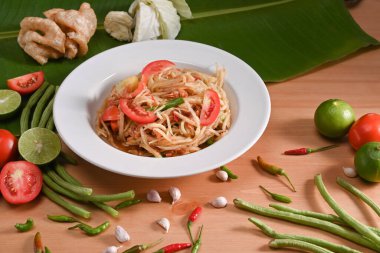 Beyaz tabakta Papaya salatası ve ahşap masada malzemeler..