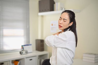 Kadın ofis çalışanı, uzun süre oturduktan ya da bilgisayar kullandıktan sonra boyun ağrısı ve sertliğini azaltmak için omuzuna masaj yapıyor..