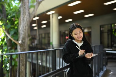 Tablet yazmak için stil kullanan mutlu öğrenci, okul koridorunda duruyor, teknoloji ve öğrenim kavramı..