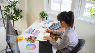 Not defterinde renkli bir logo tasarımı çizen kadın grafik tasarımcısı.