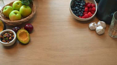 Tahta masanın etrafına yerleştirilmiş sağlıklı taze meyve, avokado, fındık ve böğürtlen..