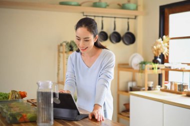 Tezgahta sağlıklı yiyecek kutuları düzenlerken tablet kullanan gülümseyen kadın..