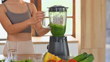 Gülümseyen kadın mutfaktaki mikserde sağlıklı yeşil bir meyve püresi hazırlıyor..