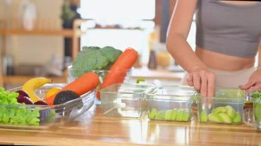 Dilimlenmiş meyve ve taze sebzeleri ahşap mutfak tezgahında yemek kabına koyan bir kadın..