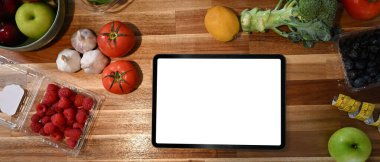 Tahta tezgahta boş beyaz ekranlı dijital tablet. Sağlıklı yaşam için taze meyve ve sebzelerle çevrili..