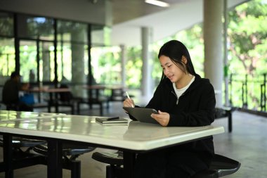 Z Geni lise öğrencisi, dijital tablet ve stilus ile doğal ışık altında açık hava sınıfında ders çalışıyor...