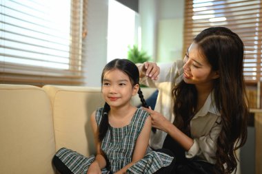 Anne kızına sevgiyle şekil veriyor kız kanepede oturuyor ve gülümsüyor, sahne mutlu ve dost canlısı..