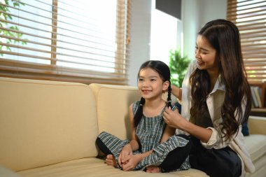 Anne kızına sevgiyle şekil veriyor kız kanepede oturuyor ve gülümsüyor, sahne mutlu ve dost canlısı..