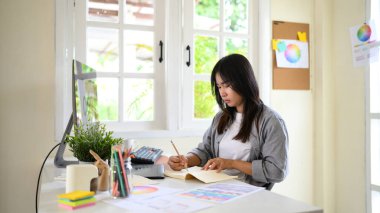Yaratıcı kadın, parlak modern çalışma alanında renk örnekleri ve araçlarla logo çizimleri tasarlıyor..
