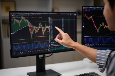 Pazar analizi sırasında bilgisayar ekranında hisse senedi grafiklerine işaret eden işlemcilerin yakın plan görüntüleri..