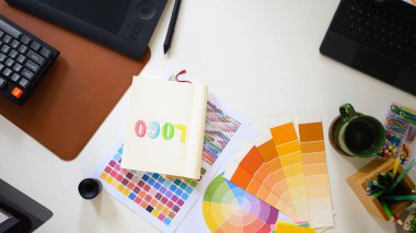 Renk paleti, dijital tablet ve not defteri çizim logosu tasarımı ile beyaz masadaki yaratıcı çalışma alanının üst görünümü.