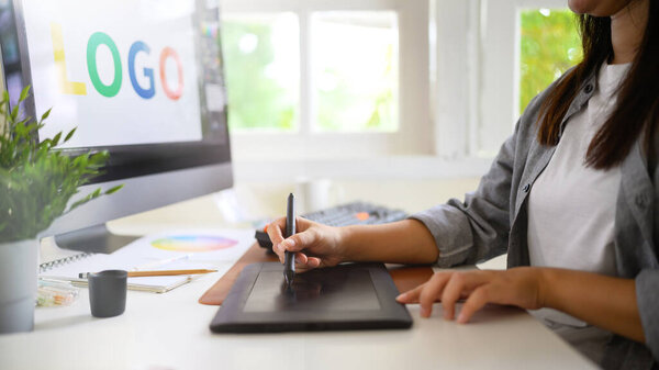 Graphic designer creating logo on digital tablet in bright modern workspace with computer and color palette.
