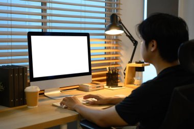 Ofisteki masaüstü bilgisayarında kahve fincanı ve sıcak ışıkla çalışan bir adam..