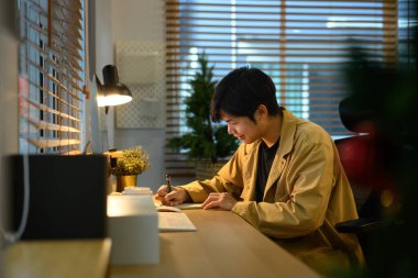 Serbest çalışan rahat ofis masasında bilgisayar ve sıcak ışık, kavram yaratıcılığı ve planlama ile notlar yazıyor..