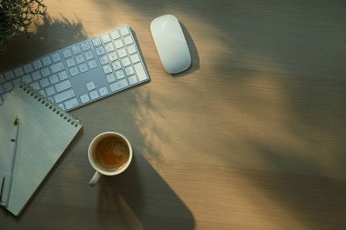 Bilgisayarlı minimalist çalışma masası, klavye, defter ve sakin günışığı gölgesi..