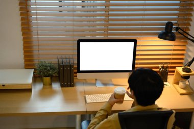 Bilgisayarda çalışan, elinde kahve fincanı olan yaratıcı bir adam..