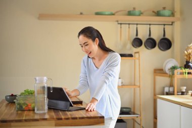 Mutfakta sağlıklı yemekler hazırlarken tablet kullanan gülümseyen kadın, yaşam tarzı dengesini ve ev yemeği pişirme ilhamını gösteriyor..