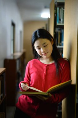 Asyalı bir kız kütüphanede kitap okuyor..