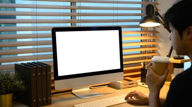 Bilgisayarda çalışan, elinde kahve fincanı olan yaratıcı bir adam..