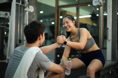 Bir kadın ve antrenörü spor salonundaki çabalarını ve takım çalışmalarını kutlamak için spor yaptıktan sonra neşeli bir tokalaşmayı paylaşıyor..