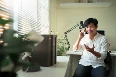 Parlak bir ev ofisinde telefonla konuşan bir adam, rahat bir iş ortamında doğal jestlerle fikirleri ifade ediyor...