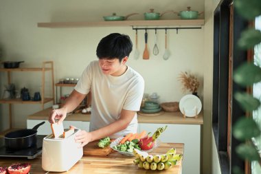 Kahvaltıyı taze malzemelerle hazırlayan ve tost makinesi kullanan bir adam..