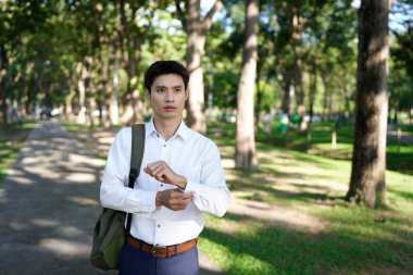 Kararlı bir ofis çalışanı parkta yürüyor, kollarını düzeltiyor, büyüme ve gelecek fırsatları arıyor..