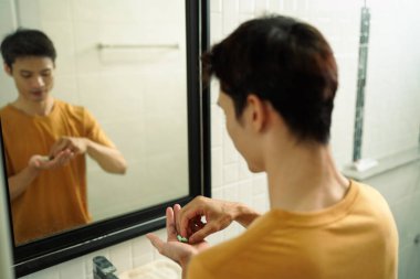 Elinde haplar olan bir adam banyo aynasında durup günlük ilaçlarını düzenli olarak almaya hazırlanıyor..