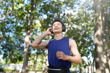 Dışarıda koşan bir adam kulaklıkla müzik dinliyor, gülümsüyor ve eğleniyor..