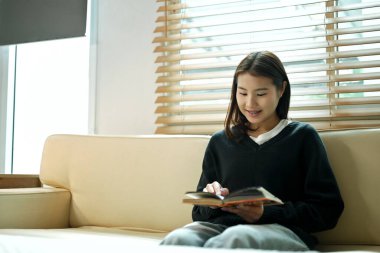 Kanepede kitap okuyan genç bir kadın evde sakin ve rahatlatıcı bir anın tadını çıkarıyor..