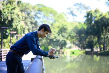 Ofisten bir adam elinde kahve fincanı olan bir gölün kenarındaki korkuluğa dayanıyor..